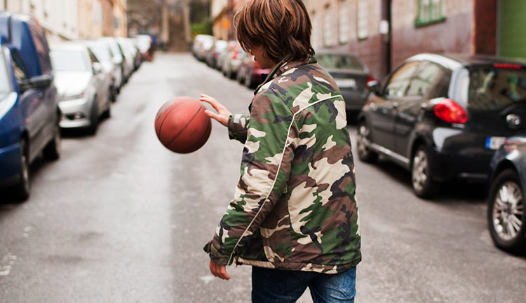 Ung pojke studsar en boll på en gata.