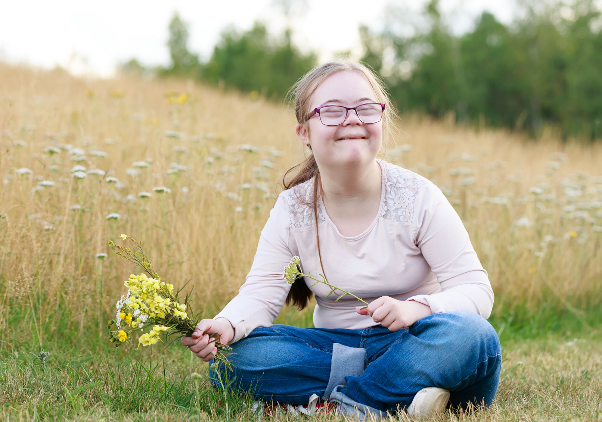 Flicka sitter på gräsmatta med blombukett i handen